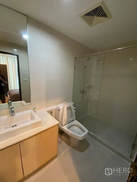 Condominium for rent or sale - Modern bathroom with large mirror, vanity, toilet and glass-enclosed shower.