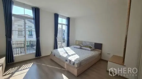 ทาวน์เฮาส์ ให้เช่าในPrawet, Bangkok - ห้องนอนใหญ่สว่าง มีหน้าต่างบานใหญ่ ม่านสีน้ำเงิน และมุมมองระเบียงเล็ก.