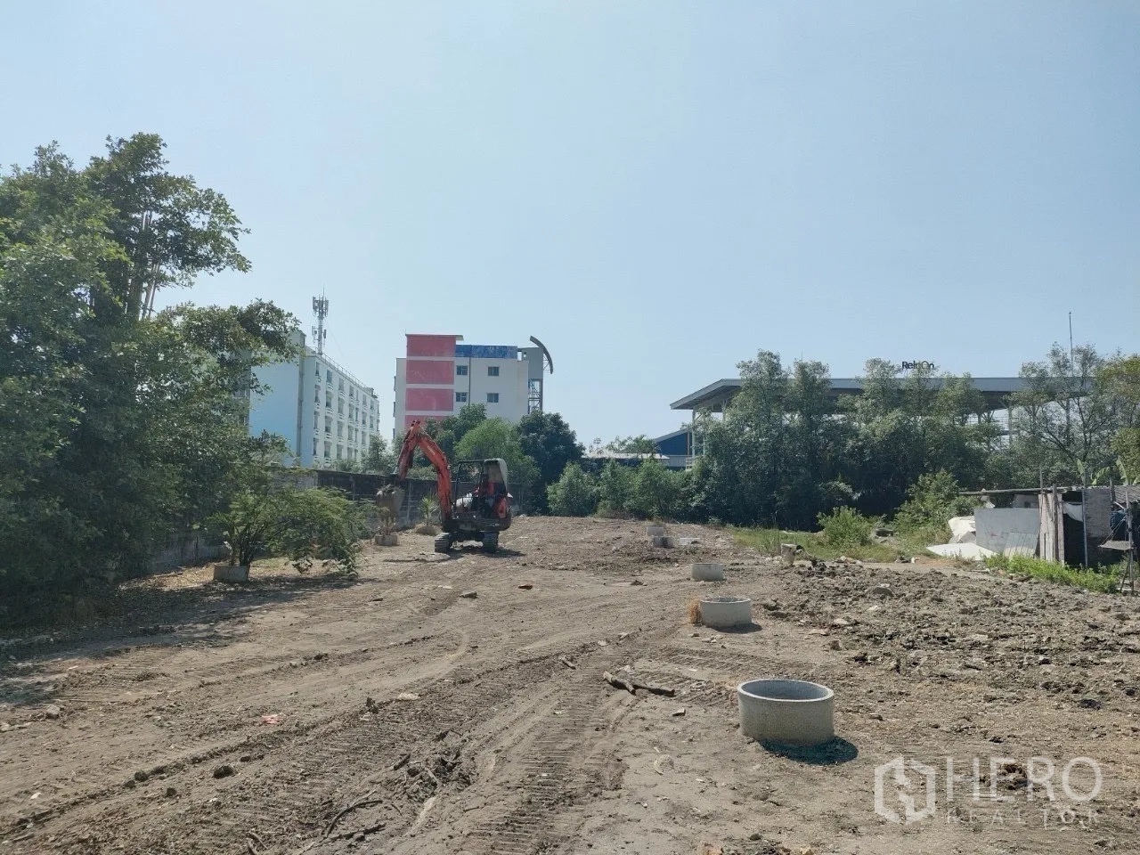 Land for sale in Mueang Samut Prakan, Samut Prakan - Construction equipment on cleared land with concrete drainage rings and mid-rise buildings behind.