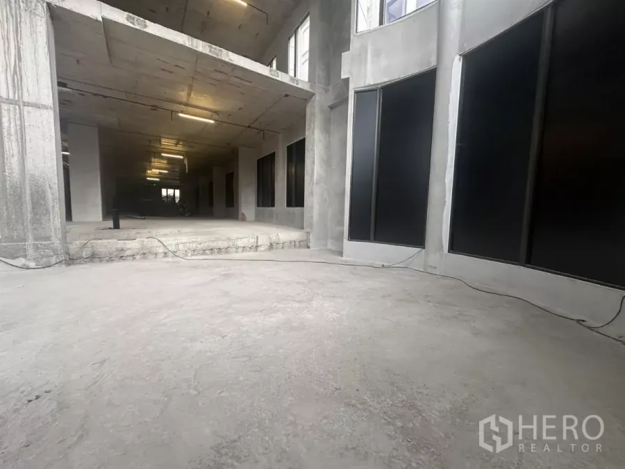 零售空间 出租在Watthana, Bangkok - 开放式一层商用空间，未完成混凝土地面与弧形玻璃立面。