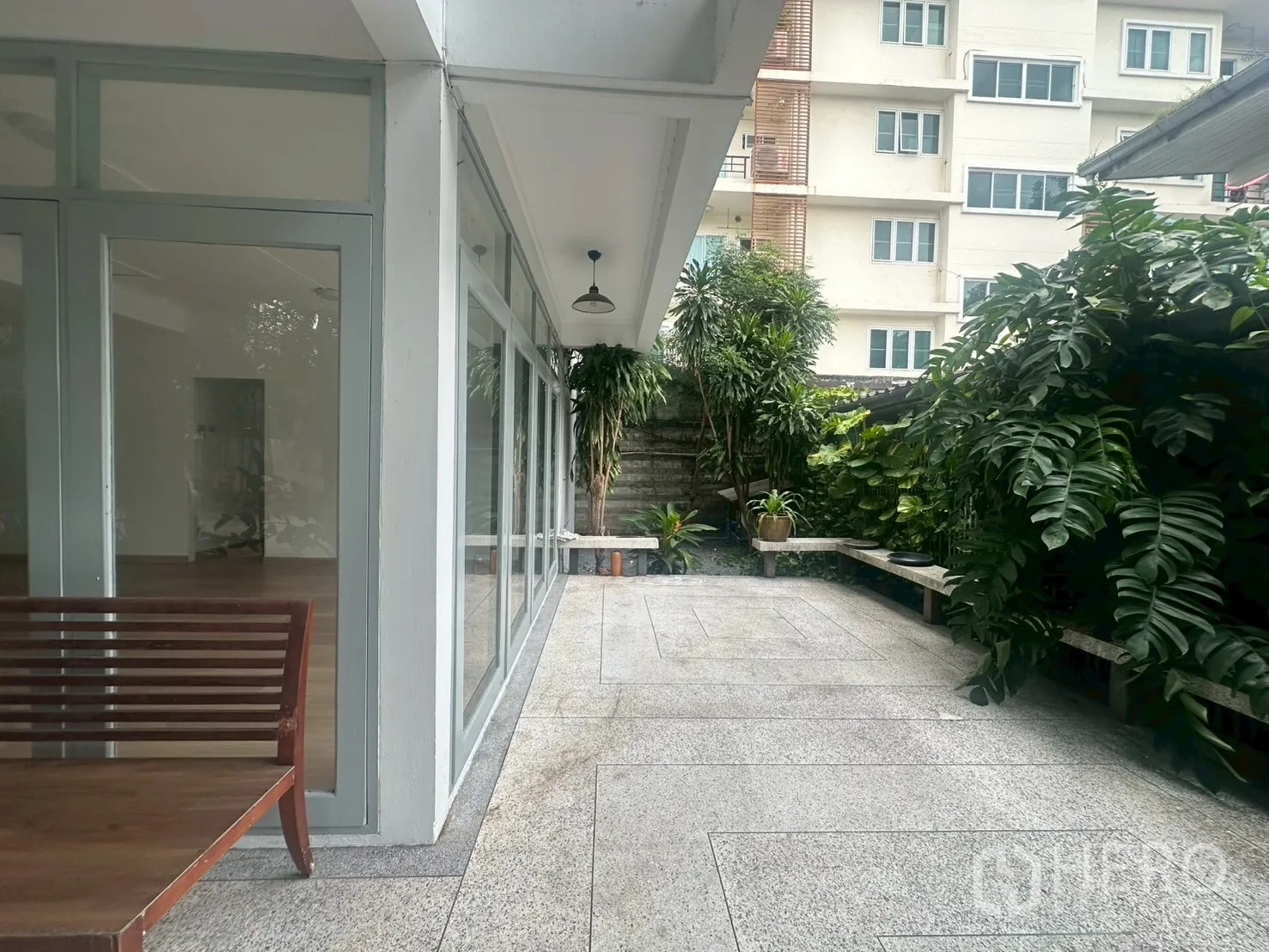 บ้าน ให้เช่าในWatthana, Bangkok - เฉลียงครึ่งในครึ่งนอก ผนังกระจกพร้อมม้านั่งและสวนเขียวชอุ่มริมรั้ว.