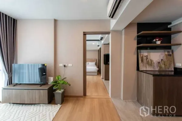 Condominium for rent in Huai Khwang, Bangkok - Bright condo living room with TV console, wood floors and doorway to a bedroom.