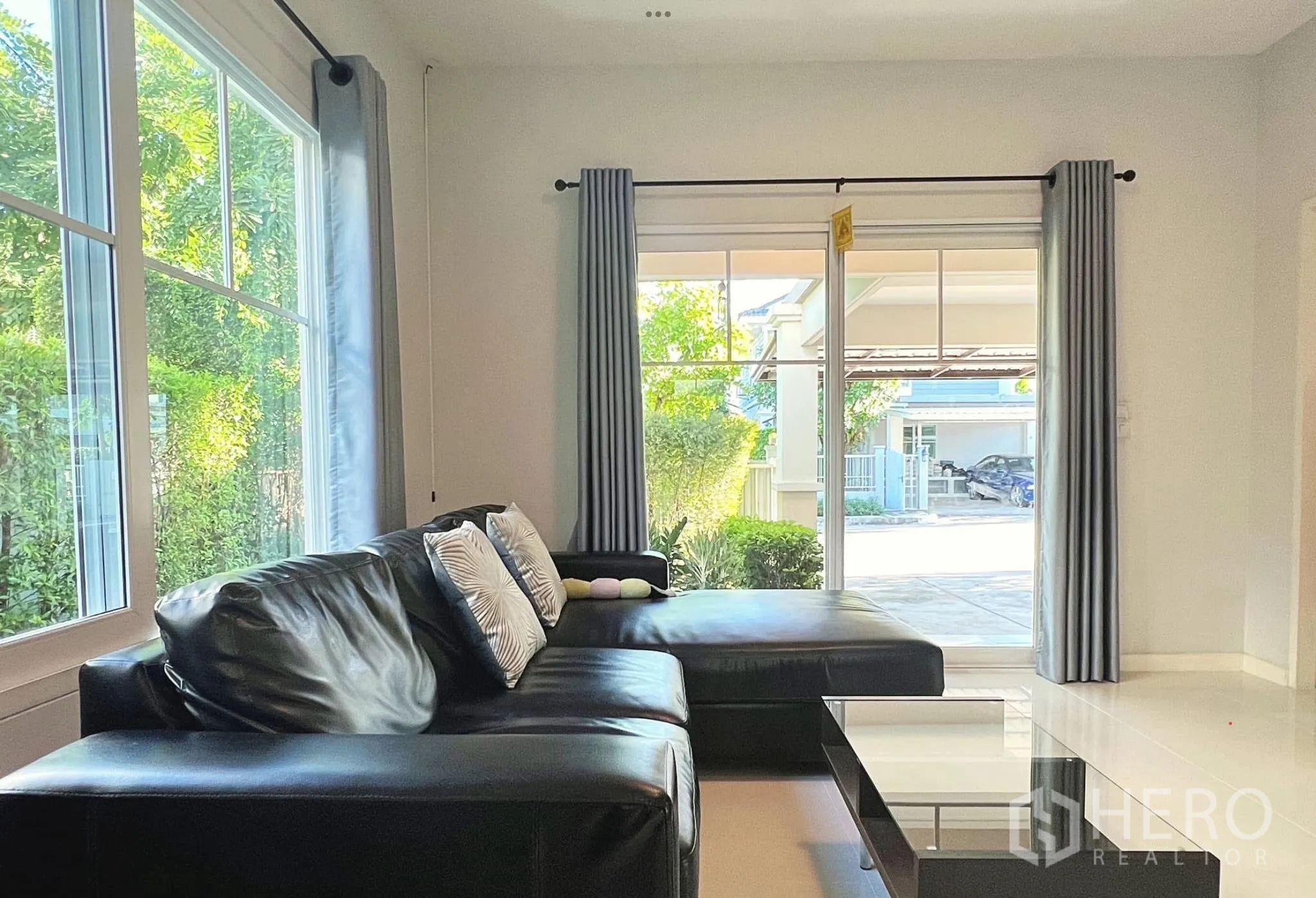 Townhouse for rent or sale in Sai Mai, Bangkok - Corner of living area showing black leather sectional sofa by sliding glass doors.