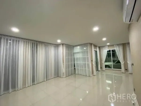 Detached House for rent in Prawet, Bangkok - Bright empty living room with glossy tiled floor, sheer curtains and recessed lighting.