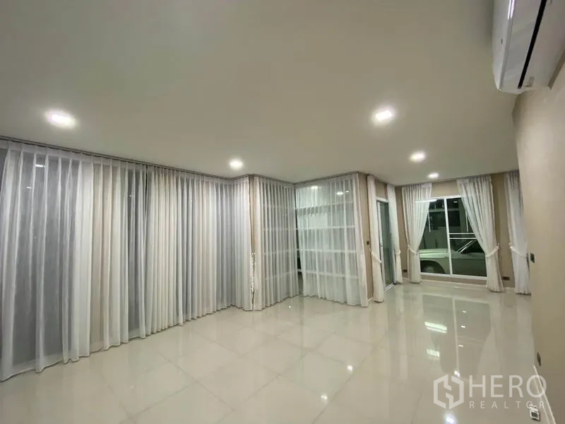 Detached House for rent in Prawet, Bangkok - Bright empty living room with glossy tiled floor, sheer curtains and recessed lighting.