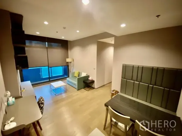 Condominium for rent or sale in Bang Rak, Bangkok - Open living and dining area with desk, roller blinds and floor-to-ceiling window bringing natural light.