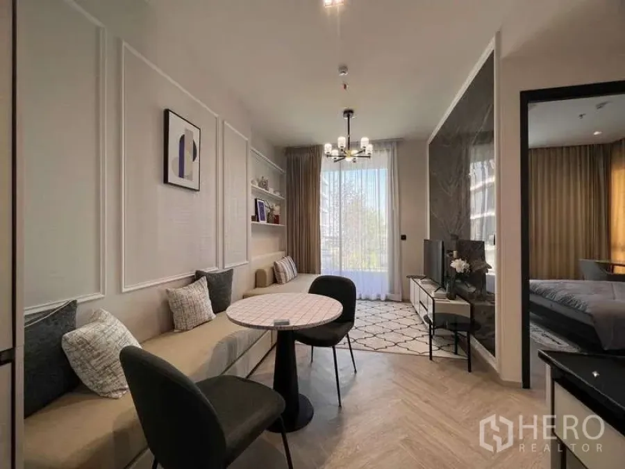 คอนโด ให้เช่า - ห้องนั่งเล่นและทานอาหารสว่าง พร้อมเบาะบิวท์อิน โต๊ะกลม ผนังทีวี และหน้าต่างสูงพร้อมม่านโปร่ง