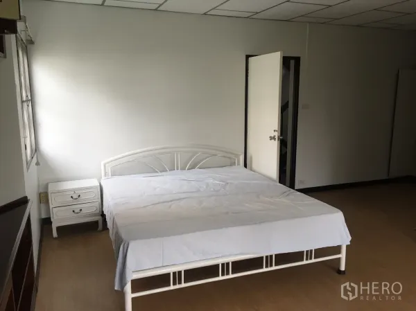Townhouse for rent in Khlong Toei, Bangkok - Spacious bedroom with white metal bedframe, bedside table, and wood flooring.