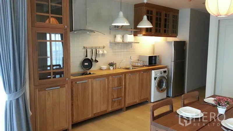 Condominium for rent or sale in Watthana, Bangkok - Built-in wooden kitchen with hob, range hood, sink, fridge, microwave, and washing machine.