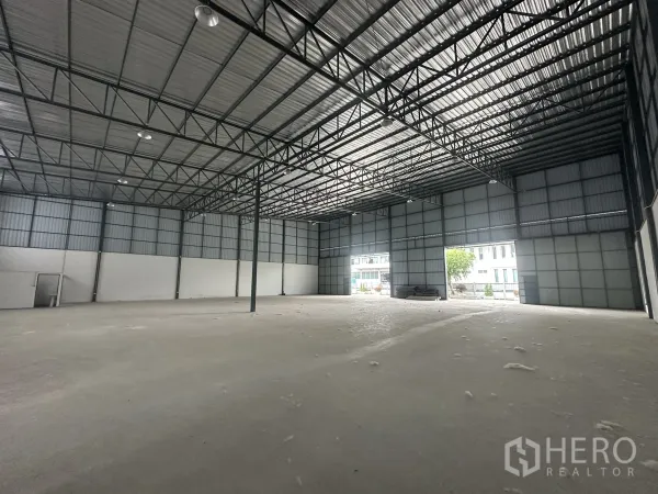 Warehouse for rent in Lam Luk Ka, Pathum Thani - Open-plan warehouse space with high ceiling, two large shutter doors and bright natural light.