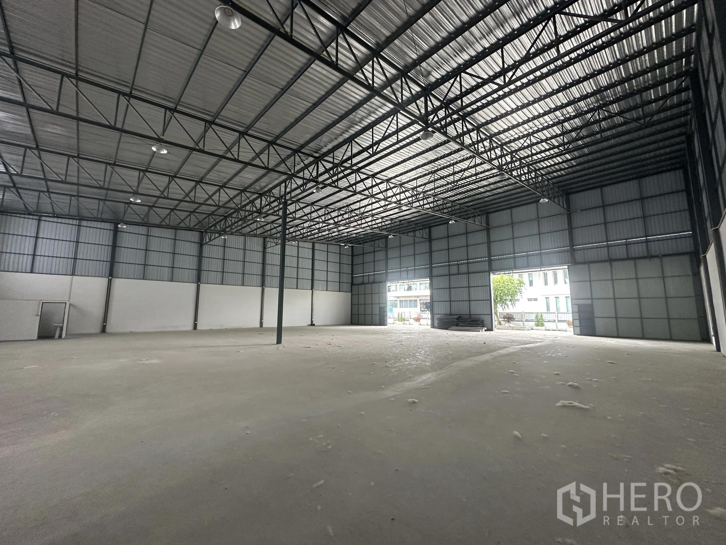 Warehouse for rent in Lam Luk Ka, Pathum Thani - Open-plan warehouse space with high ceiling, two large shutter doors and bright natural light.