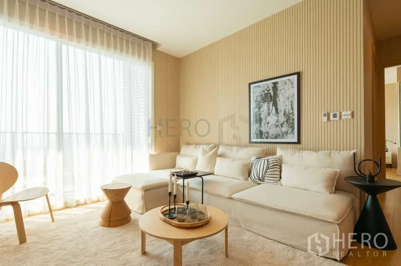 Condominium for sale in Khlong Toei, Bangkok - Cozy lounge with L-shaped sofa, coffee tables, and tall curtains allowing natural light.