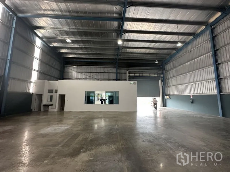 โรงงาน ให้เช่าในBang Phli, Samut Prakan - ฮอลล์โกดังโล่ง มีบล็อกออฟฟิศสีขาวตรงกลาง ไฟ LED สว่าง และประตูม้วนขนาดใหญ่