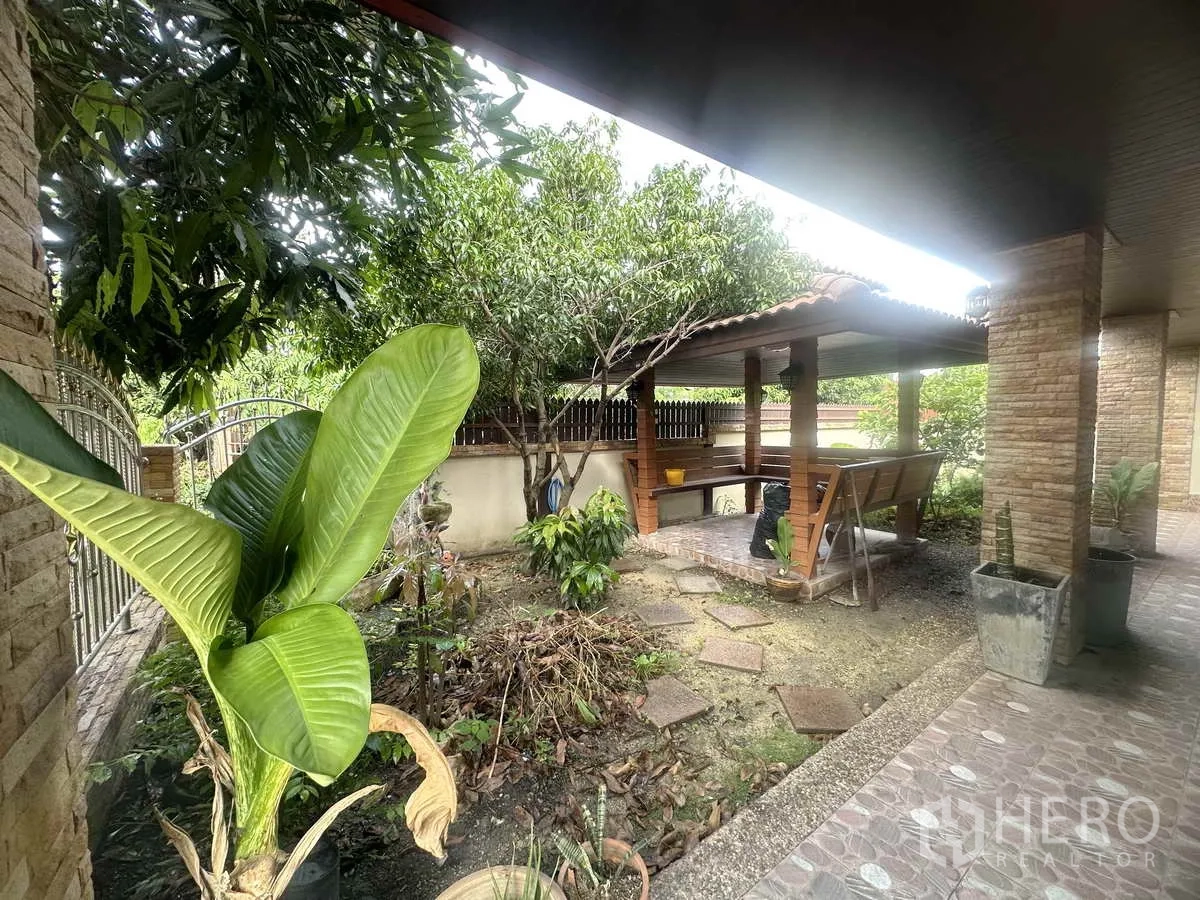 独立式住宅 出售在Pathum Thani - 前花园中的遮阳凉亭，配长椅，周围树木葱郁。