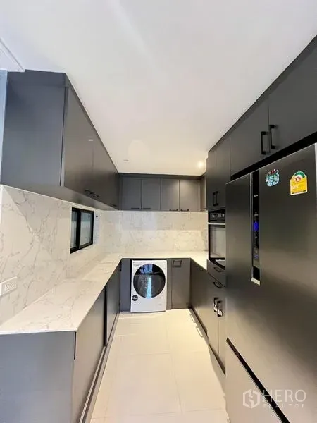 Townhouse for rent in Saphan Sung, Bangkok - Sleek galley kitchen with matte cabinets, marble-look counters, large refrigerator and washer-dryer.
