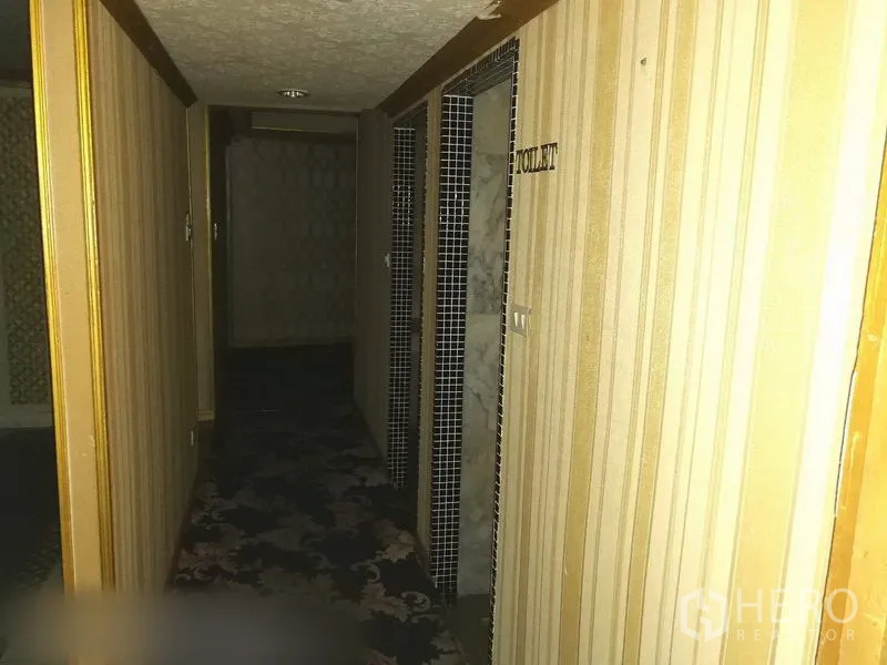 零售空间 出租在Khlong Toei, Bangkok - 带条纹墙面的走廊，通往铺砖的卫生间隔间。