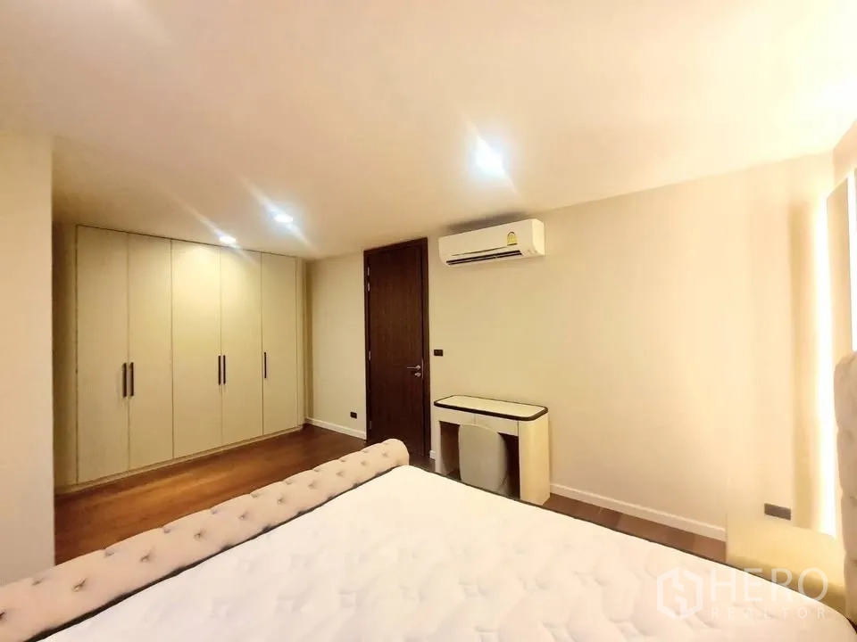 Townhouse for rent or sale in Watthana, Bangkok - Bedroom with built-in wardrobes, air conditioner, desk, and upholstered bed.