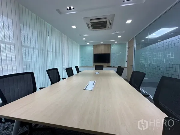 Office Space for rent - Bright meeting room with a long conference table, ergonomic chairs, ceiling cassette AC, TV wall and glass partitions.