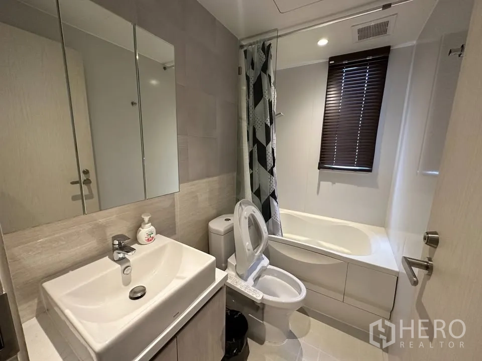 公寓 for rent in Watthana, Bangkok - 现代卫浴含洗手台、镜柜、坐便与带窗浴缸及浴帘。