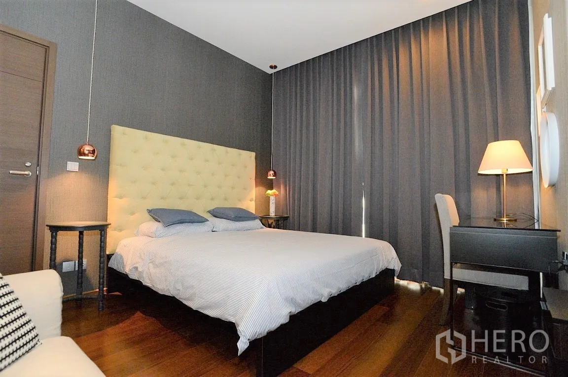 Condominium for rent in Watthana, Bangkok - Spacious bedroom with desk, bedside lamps, and floor-to-ceiling blackout curtains.