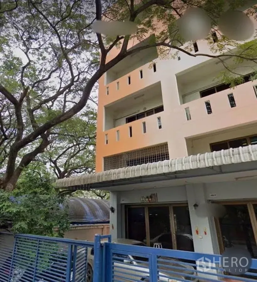 ทาวน์เฮาส์ ขายในWang Thonglang, Bangkok - ด้านหน้าทาวน์เฮ้าส์ 4 ชั้น มีระเบียง รั้วเหล็กสีน้ำเงิน และต้นไม้ใหญ่ ในเขตวังทองหลาง กรุงเทพฯ