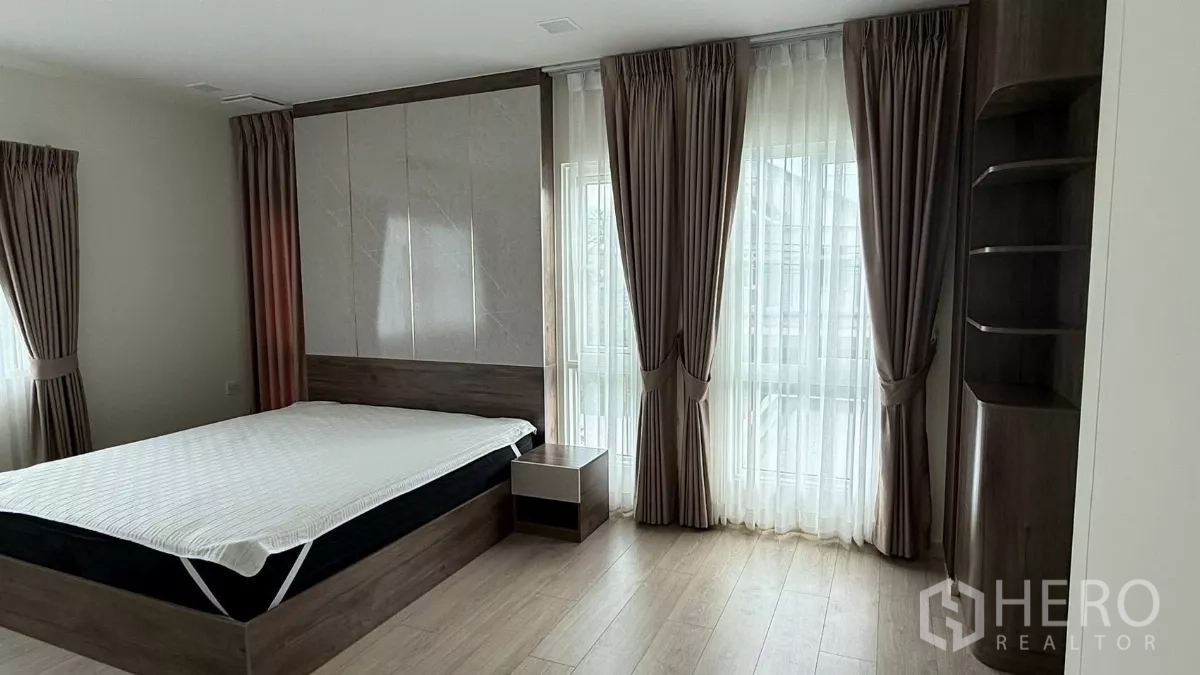 บ้าน ให้เช่าในBang Phli, Samut Prakan - มุมห้องนอนหลักพร้อมหน้าต่างบานใหญ่ ม่านโปร่ง และโต๊ะข้างเตียง.