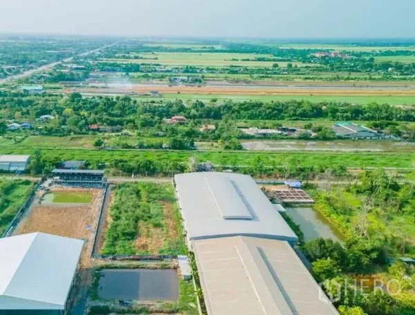 Land for sale in Khlong Luang, Pathum Thani - Aerial view of canal-side land plot in Khlong Luang, Pathum Thani, beside warehouses and green fields.