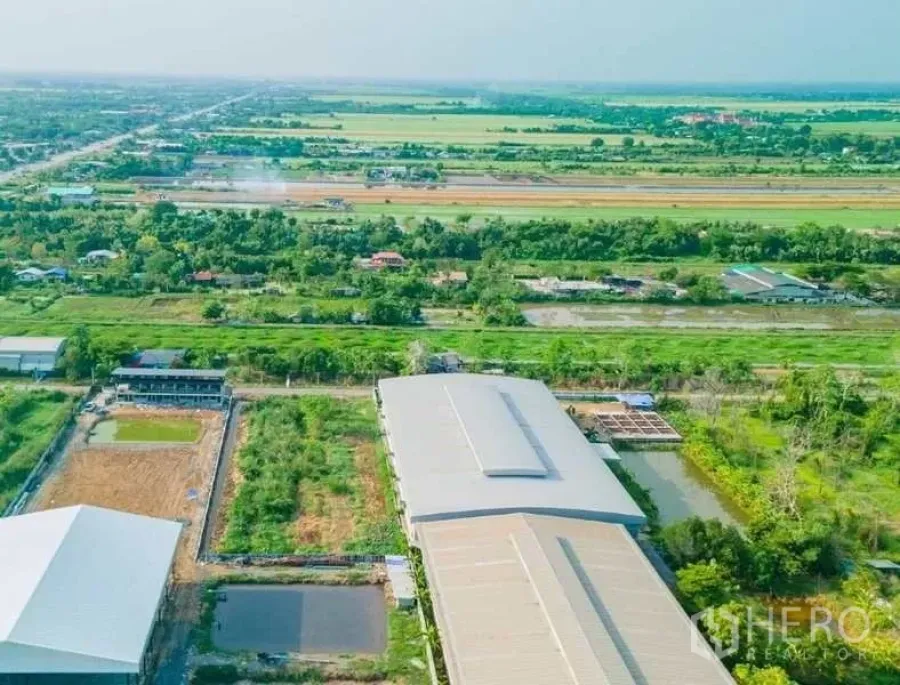 Land for sale in Khlong Luang, Pathum Thani - Aerial view of canal-side land plot in Khlong Luang, Pathum Thani, beside warehouses and green fields.