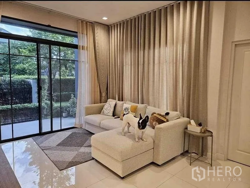 บ้าน ขายในBang Kruai, Nonthaburi - ห้องนั่งเล่นสว่าง โซฟารูปตัวแอล ผ้าม่านเต็มผนัง และประตูกระจกออกลาน
