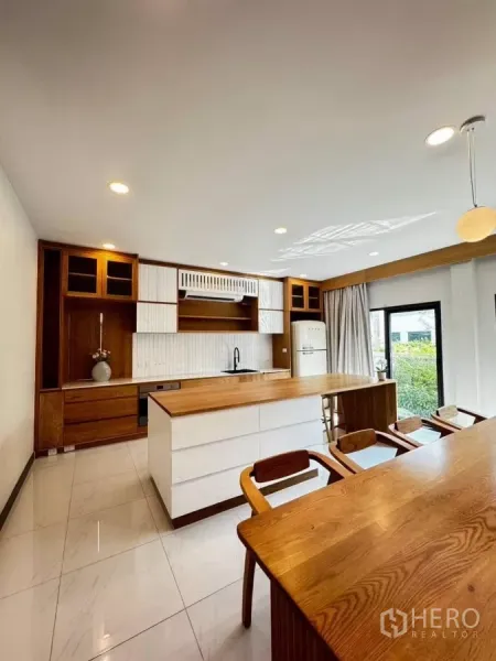 Detached House for rent or sale in Bang Phli, Samut Prakan - Open‑plan Western kitchen with island, wood and white cabinetry, bar seating, and a door to the garden.