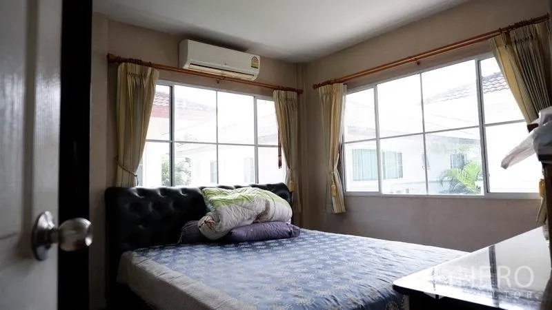Detached House for rent in Prawet, Bangkok - Secondary bedroom with corner windows, curtains and a wall-mounted air conditioner.