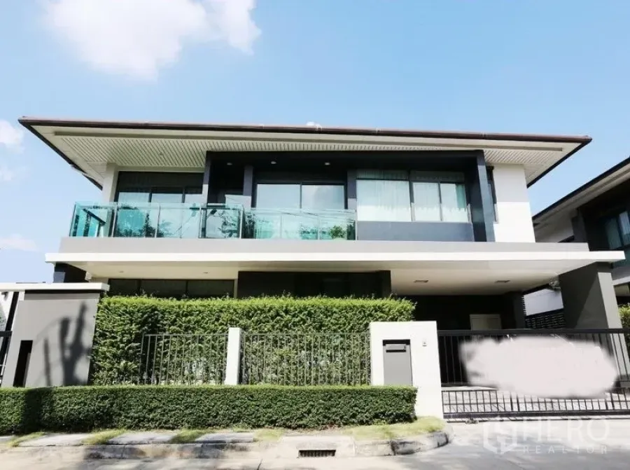 Detached House for rent or sale in Bang Kapi, Bangkok - Modern two-storey detached house with glass balcony, tall hedge and gated carport in Bang Kapi under a clear sky.