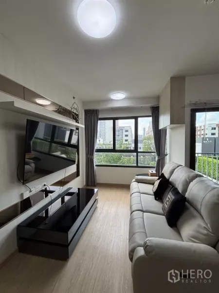 Condominium for rent in Phra Khanong, Bangkok - Bright condo lounge with wall-mounted TV, large windows and city outlook in Phra Khanong, Bangkok.