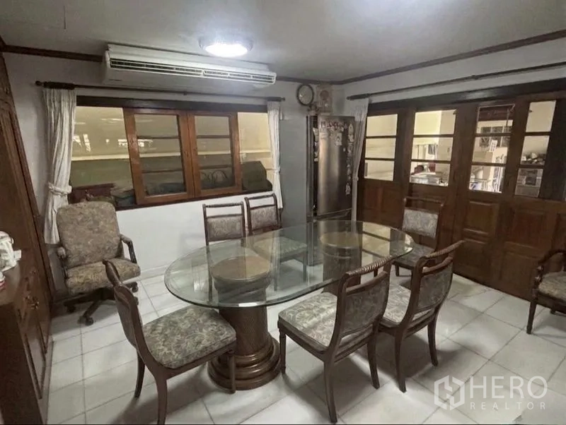 独栋房屋 for sale in Suan Luang, Bangkok - 餐厅设圆形玻璃餐桌、六把椅子和木质推拉门。