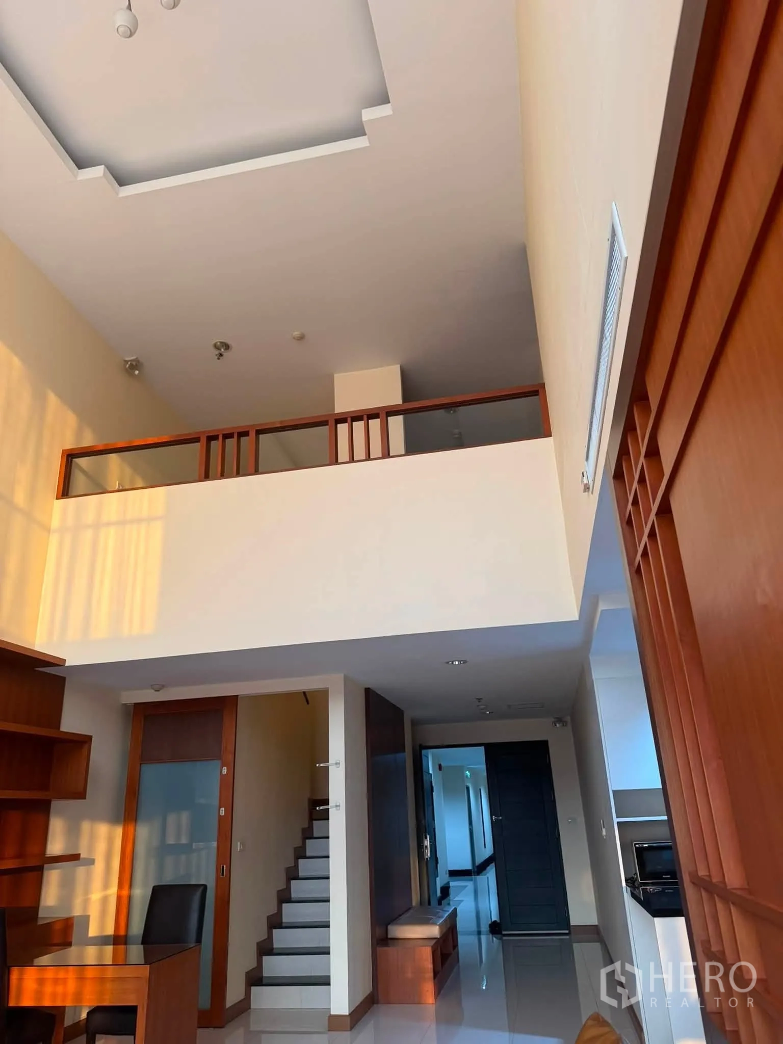 Condominium for rent in Khlong Toei, Bangkok - Staircase to a mezzanine level under a high ceiling with built-in shelving and entry hall.