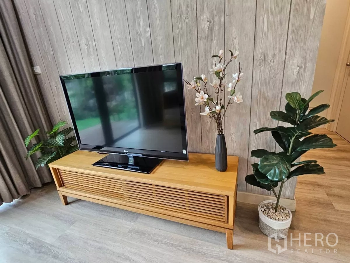 Detached House for rent or sale in Don Mueang, Bangkok - Close-up of wooden TV stand with potted plants against a wood panel feature wall.