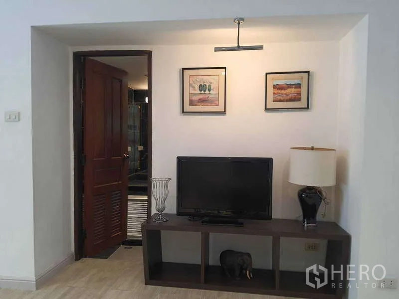 ทาวน์เฮาส์ ให้เช่าในKhlong Toei, Bangkok - มุมนั่งดูทีวีพร้อมกรอบรูปและประตูไม้สู่ห้องน้ำ