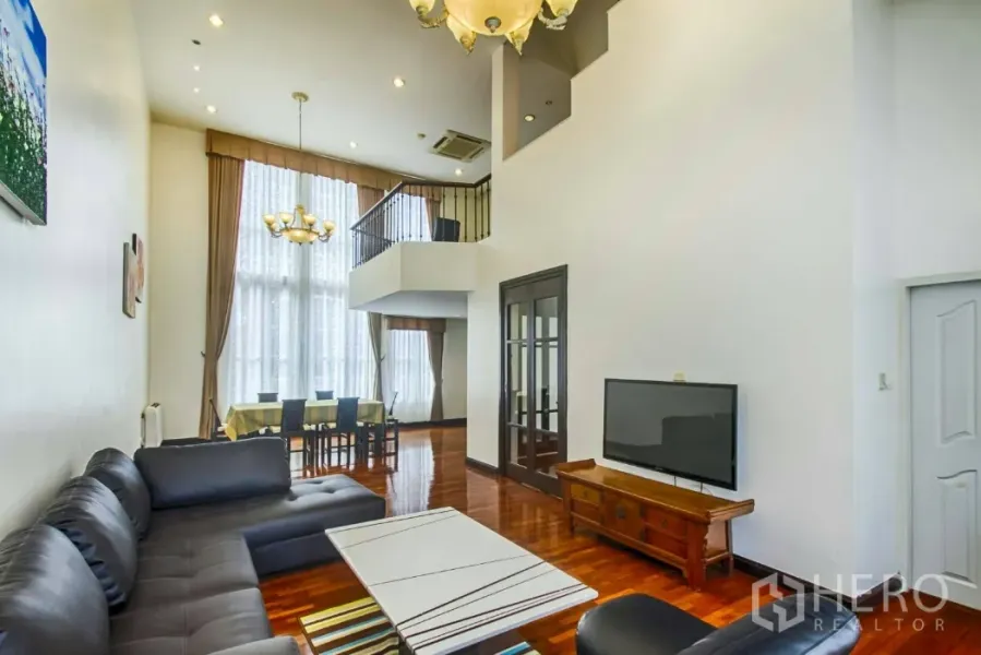 Townhouse for rent in Watthana, Bangkok - Spacious living room with double-height ceiling, chandelier and floor-to-ceiling windows.
