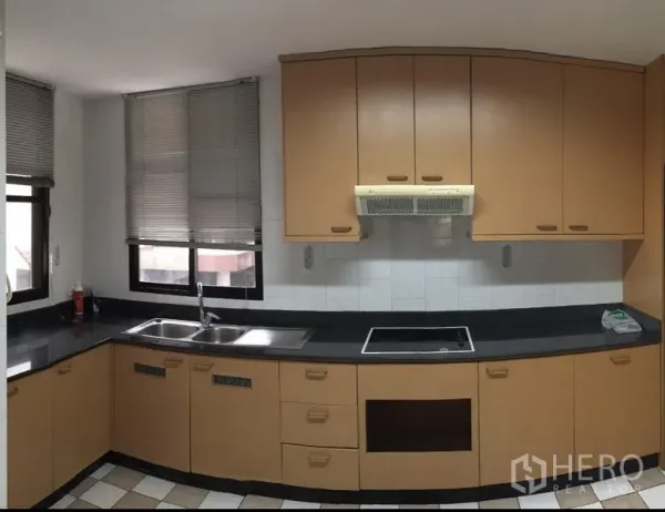 Condominium for rent in Watthana, Bangkok - L-shaped kitchen with black countertops, double sink, electric cooktop, exhaust hood and two windows with blinds.