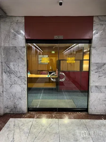 办公空间 出租 - 走廊视角的玻璃门办公室，内有接待区与不锈钢把手。