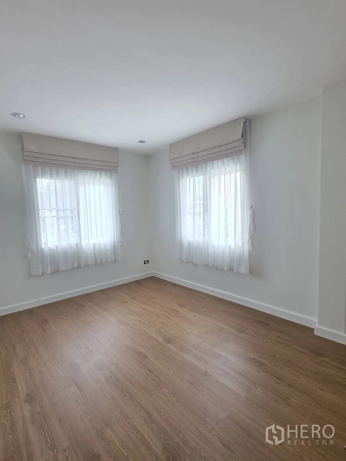 Detached House for sale in Lam Luk Ka, Pathum Thani - Bright bedroom with twin windows and light wood flooring.
