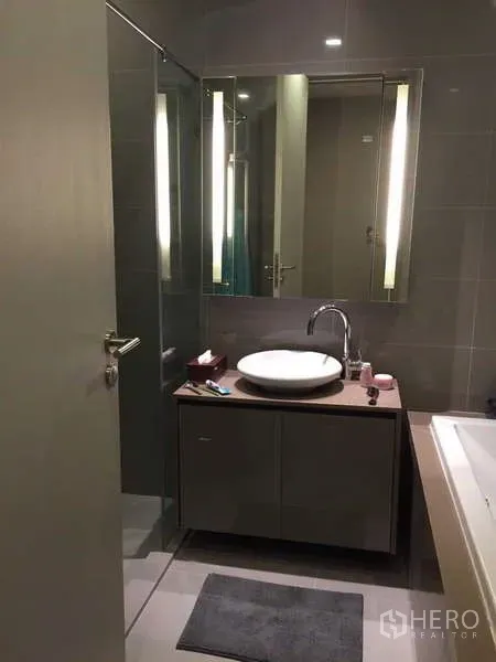 Condominium for rent in Bang Rak, Bangkok - Modern bathroom with round basin, backlit mirror and glass shower enclosure.