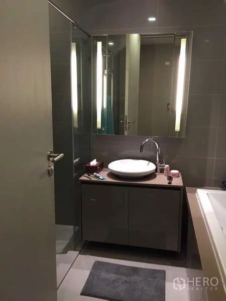 Condominium for rent in Bang Rak, Bangkok - Modern bathroom with round basin, backlit mirror and glass shower enclosure.