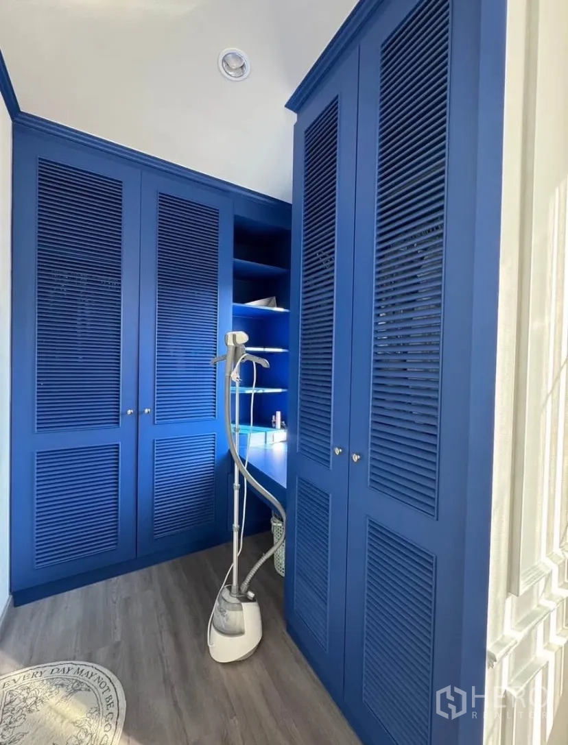 บ้านเดี่ยว for rent or sale in Lat Krabang, Bangkok - ห้องแต่งตัวบิลท์อินสีน้ำเงิน ตู้เสื้อผ้าบานเกล็ด ชั้นวางของ และเครื่องสตีมผ้า พื้นลายไม้
