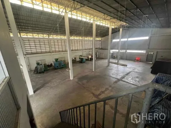 Warehouse for rent in Lam Luk Ka, Pathum Thani - Spacious high-ceiling warehouse floor with steel columns, louvered ventilation, and machines along the walls.