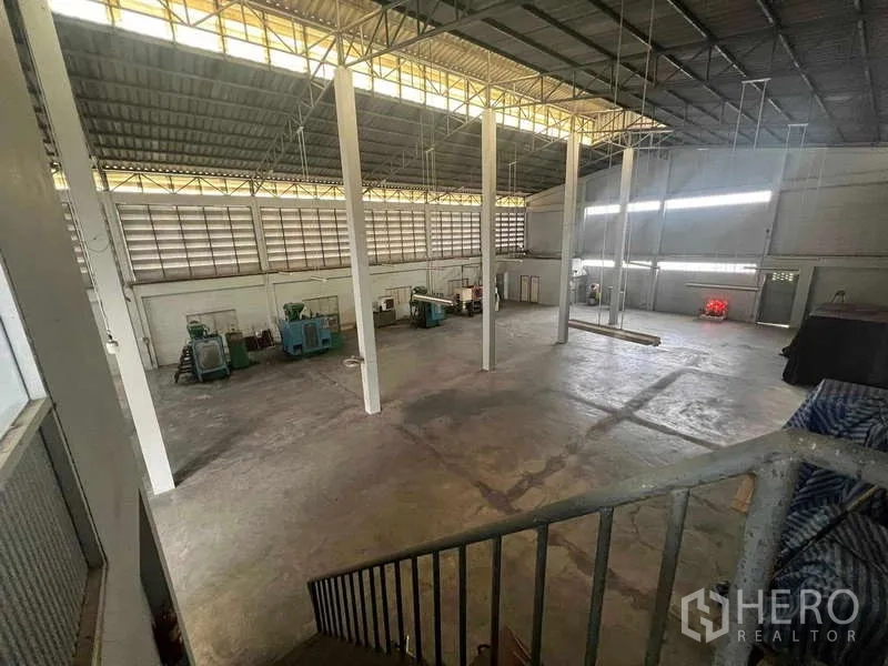 Warehouse for rent in Lam Luk Ka, Pathum Thani - Spacious high-ceiling warehouse floor with steel columns, louvered ventilation, and machines along the walls.