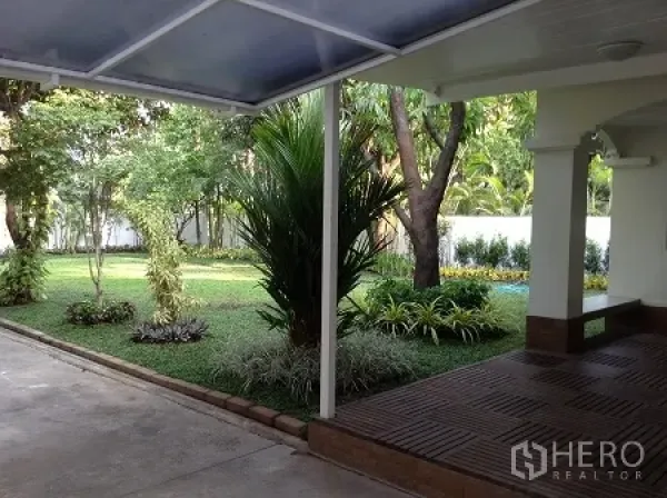 Detached House for rent in Ratchathewi, Bangkok - Covered terrace and driveway overlooking a landscaped lawn with tropical plants and trees.