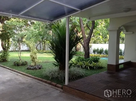 Detached House for rent in Ratchathewi, Bangkok - Covered terrace and driveway overlooking a landscaped lawn with tropical plants and trees.