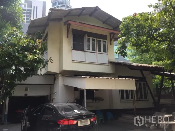 Detached House for rent in Khlong Toei, Bangkok - Front exterior of a two-storey detached house with driveway and carport under trees in Khlong Toei, Bangkok.