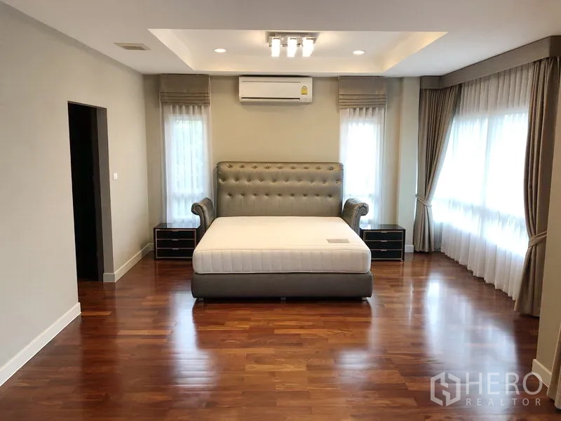 Detached House for rent or sale in Saphan Sung, Bangkok - Spacious master bedroom with large bed, corner windows, wood floors and air conditioner.